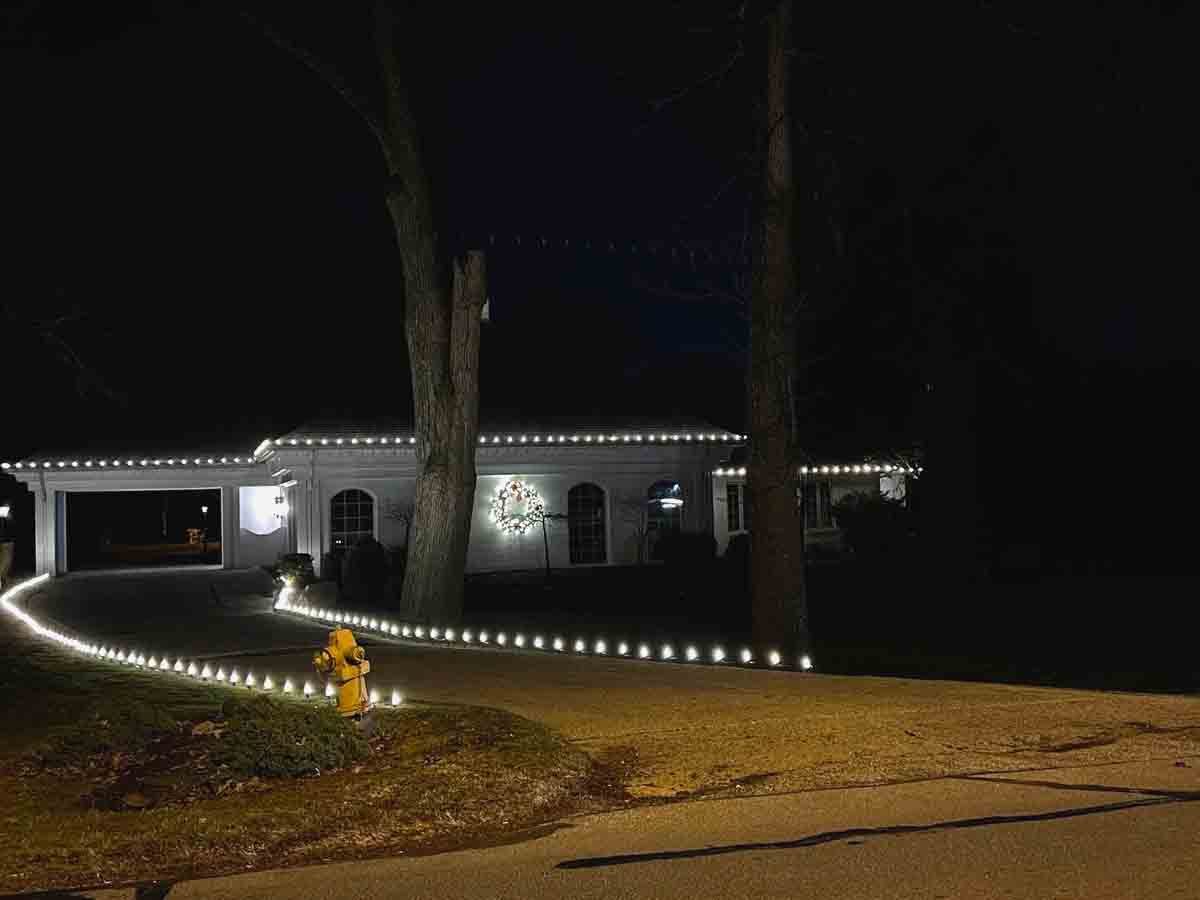 Warm white Christmas lights following the curve of a driveway and garden edge at night