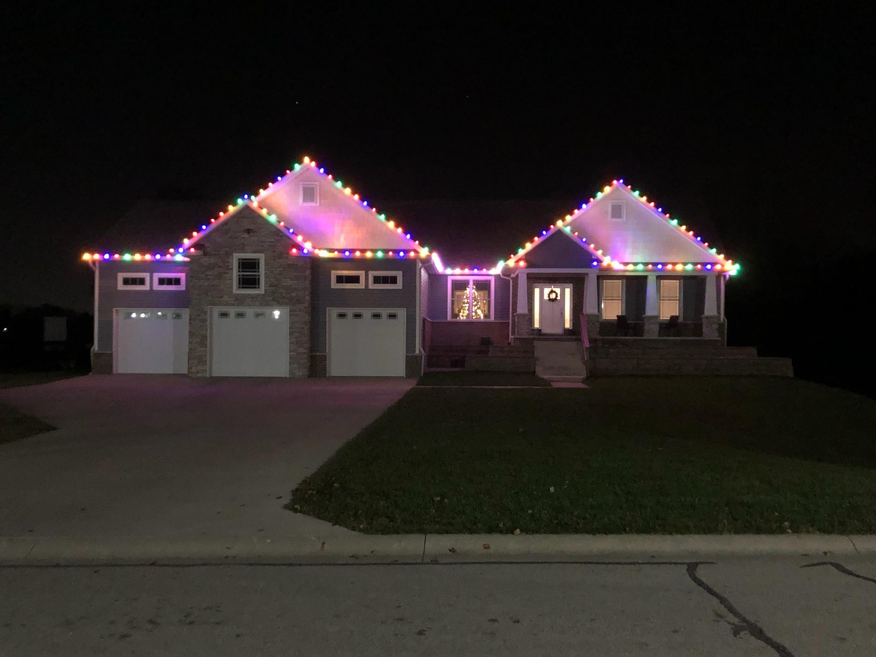 Indiana ranch home outlined in multicolor Christmas lights along both front gables and the porch roofline