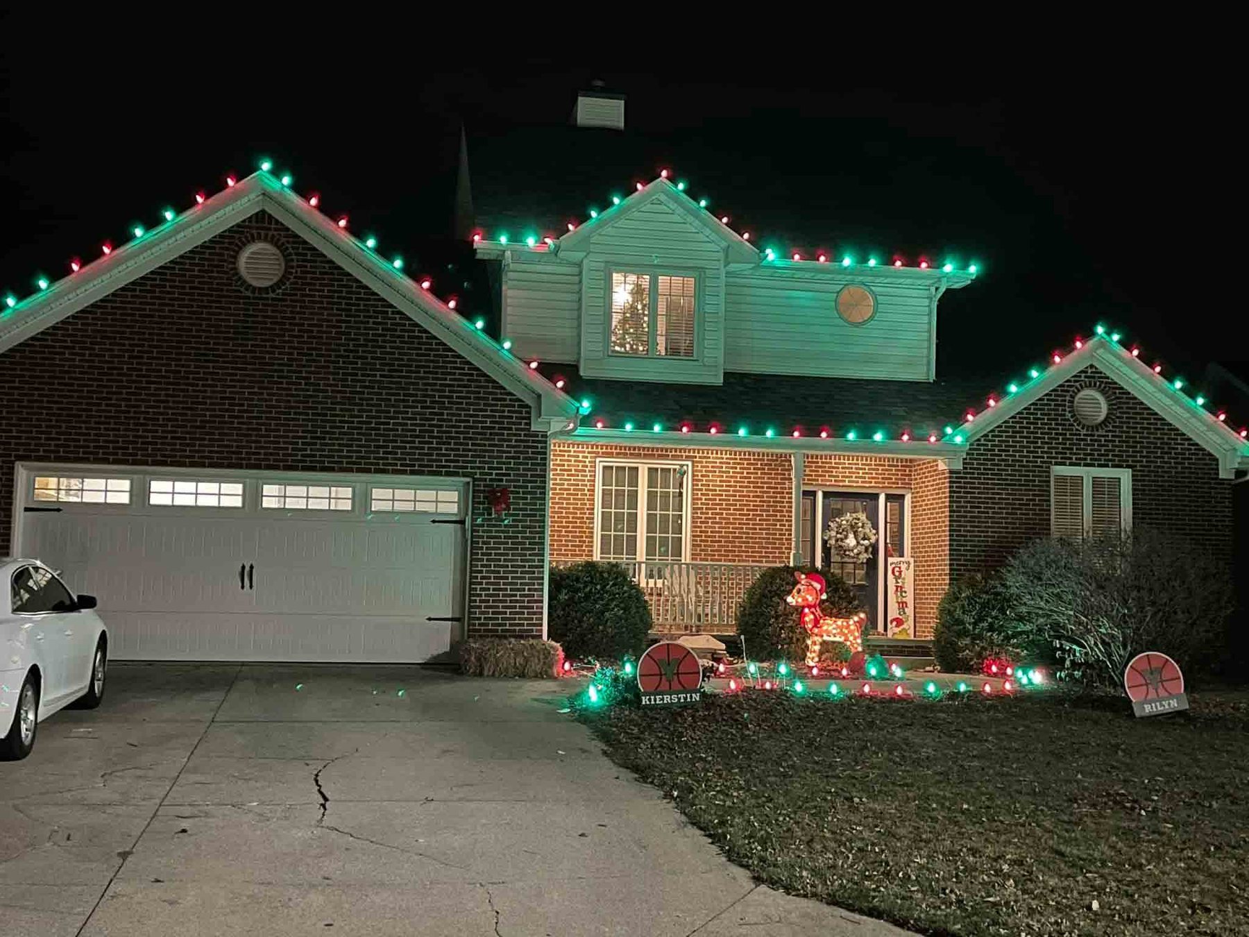 Indiana ranch home outlined in red and green Christmas lights with lighted decorations along the drive