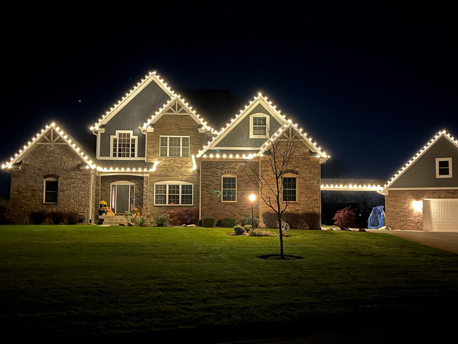 Brick and shake Indiana home with warm white Christmas lights tracing five separate roof peaks and the garage wing